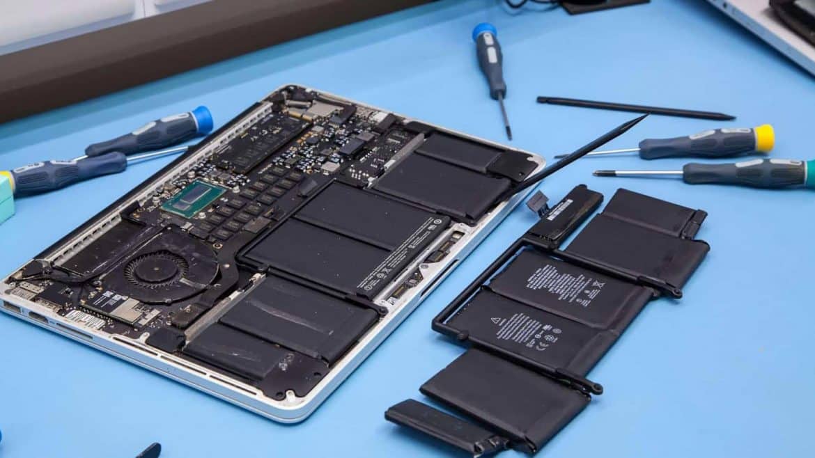 MacBook battery replacement with the old battery removed beside an open MacBook